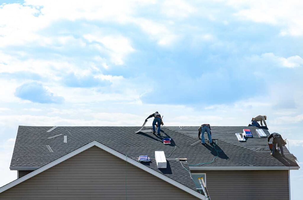 Roofing materials, underlayment, and a Class A fire-rating label arranged on a workbench beside roof sheathing.